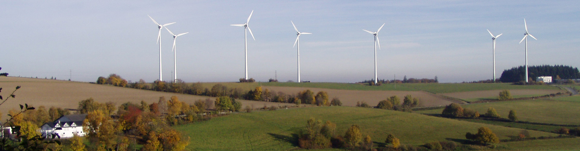Landschaft mit Wiesen, Feldern, Windrädern und Häusern an klarem Herbsttag