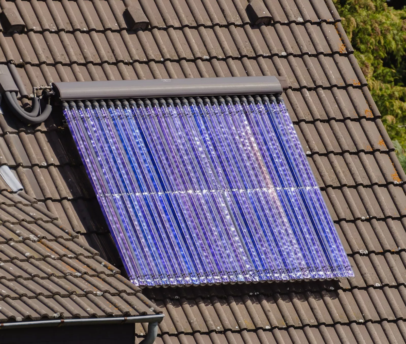 Solarthermie-Kollektor mit Vakuumröhren zur Warmwasserbereitung auf einem Ziegeldach eines Wohnhauses